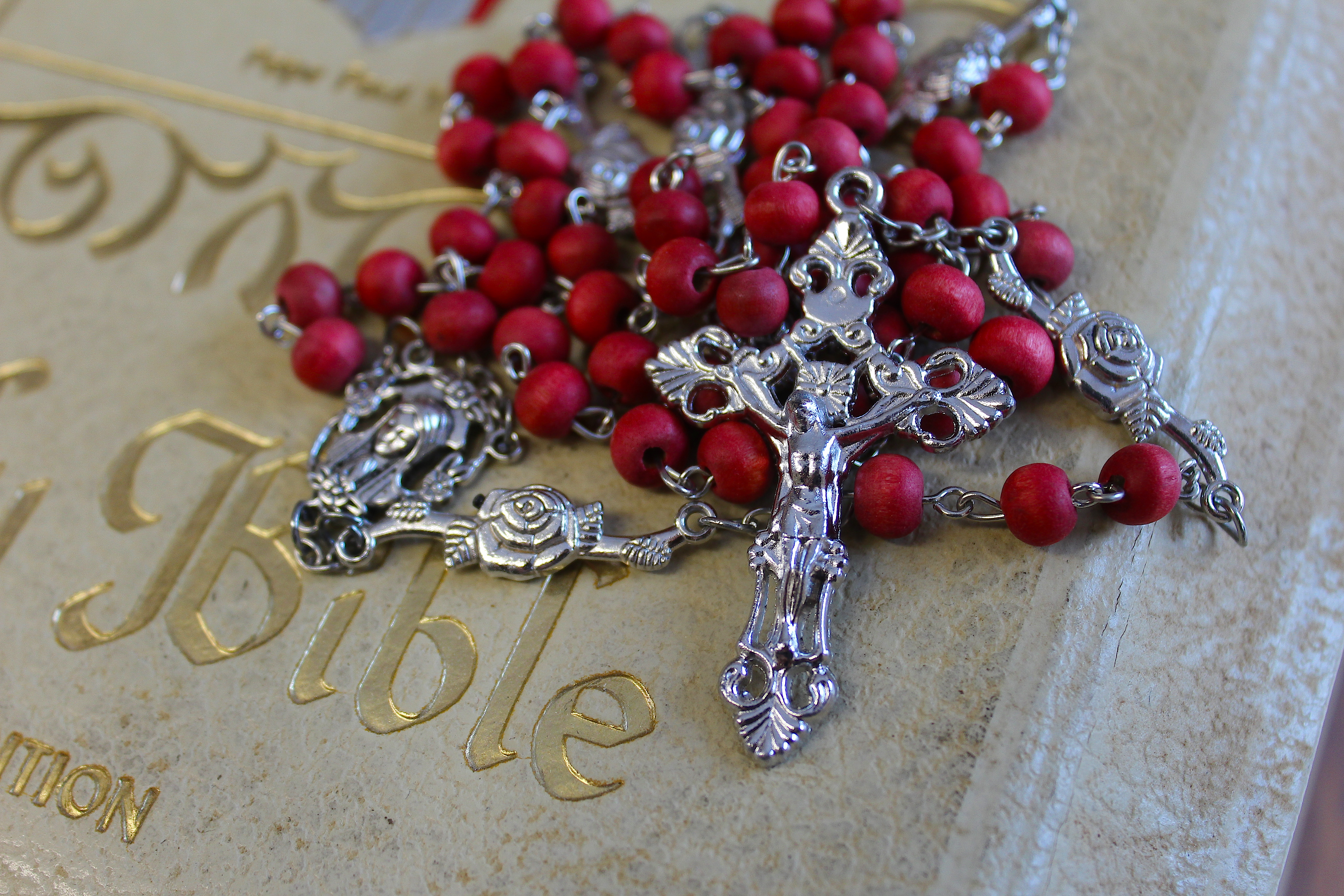 Red bead rosary with silver crucifix and silver details on a vintage white bible with gold lettering