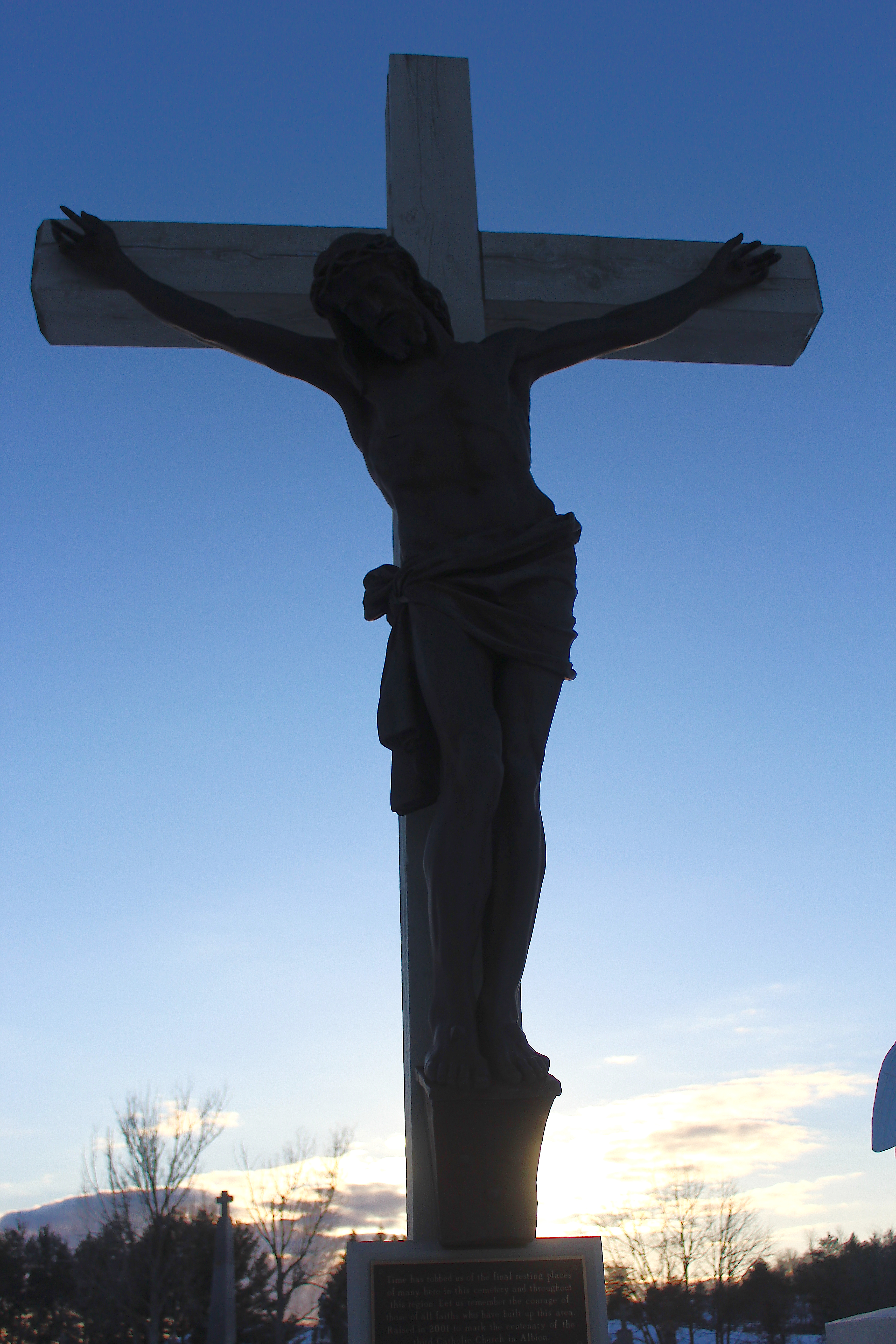 Outdoor picture of a large wooden crucifix, dark with setting sun lighting it from behind