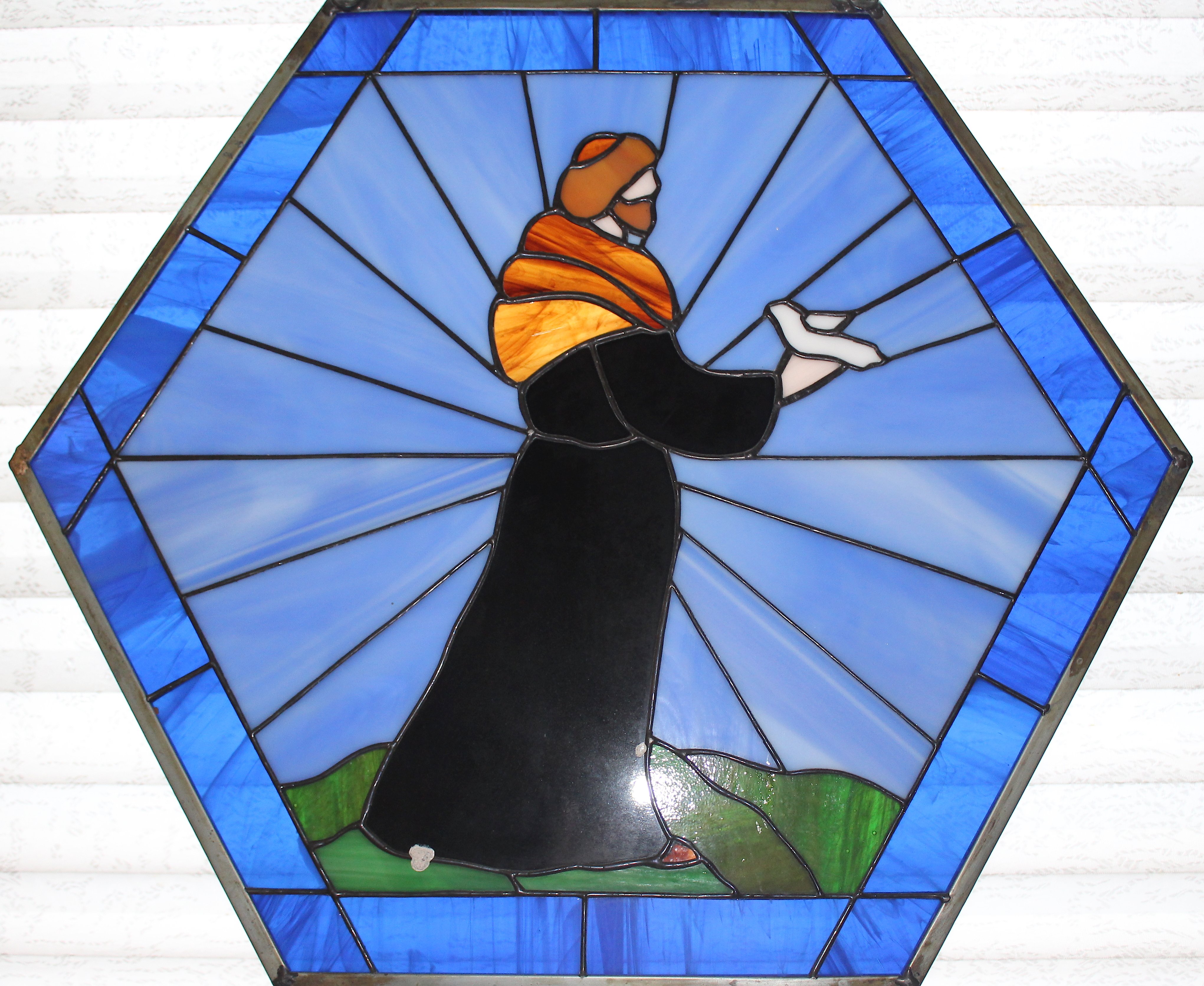 Hexagonal stained glass picture of a monk in a brown robe holding a dove