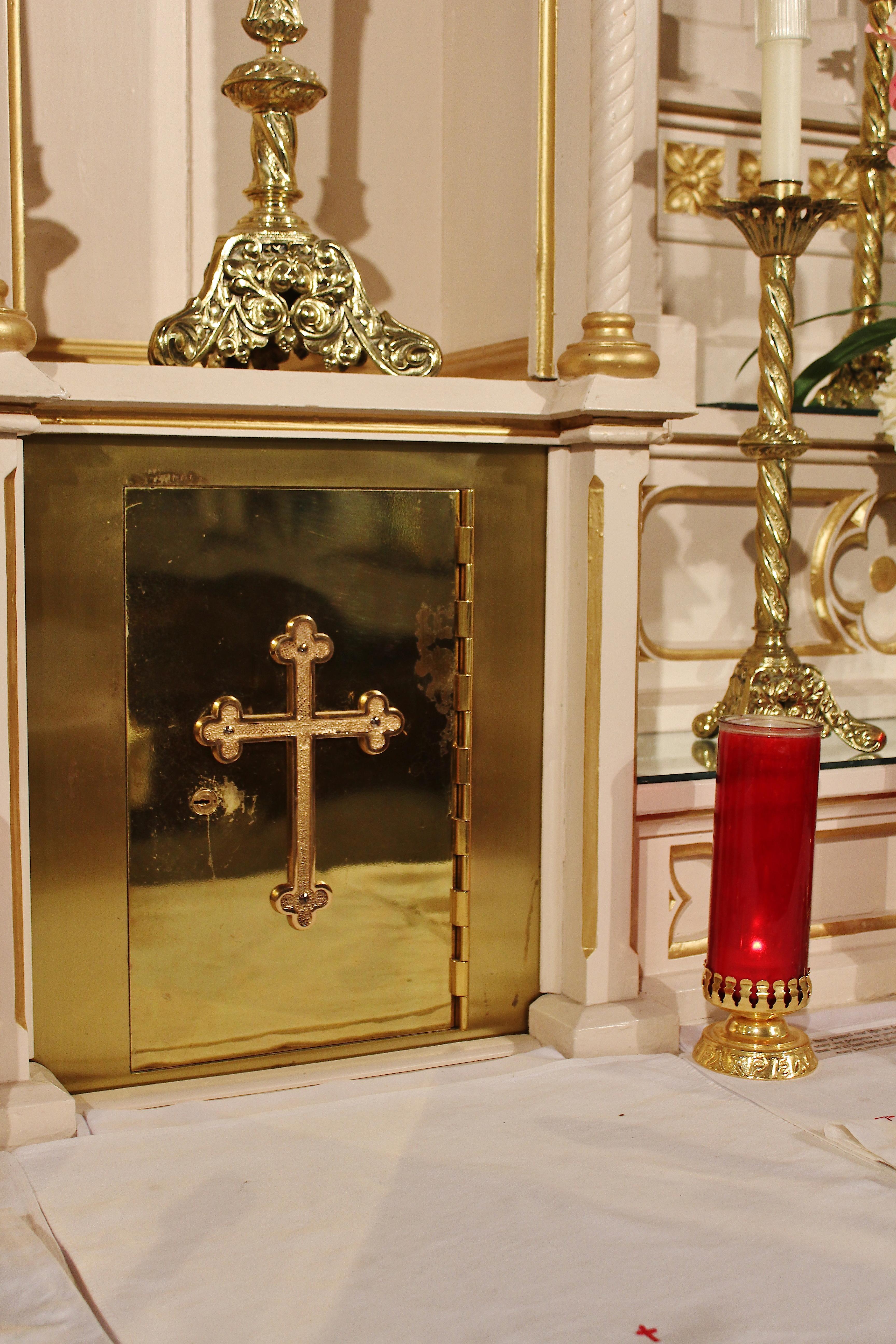 Gold Tabernacle door with a gold cross on it and a red galss candle in front